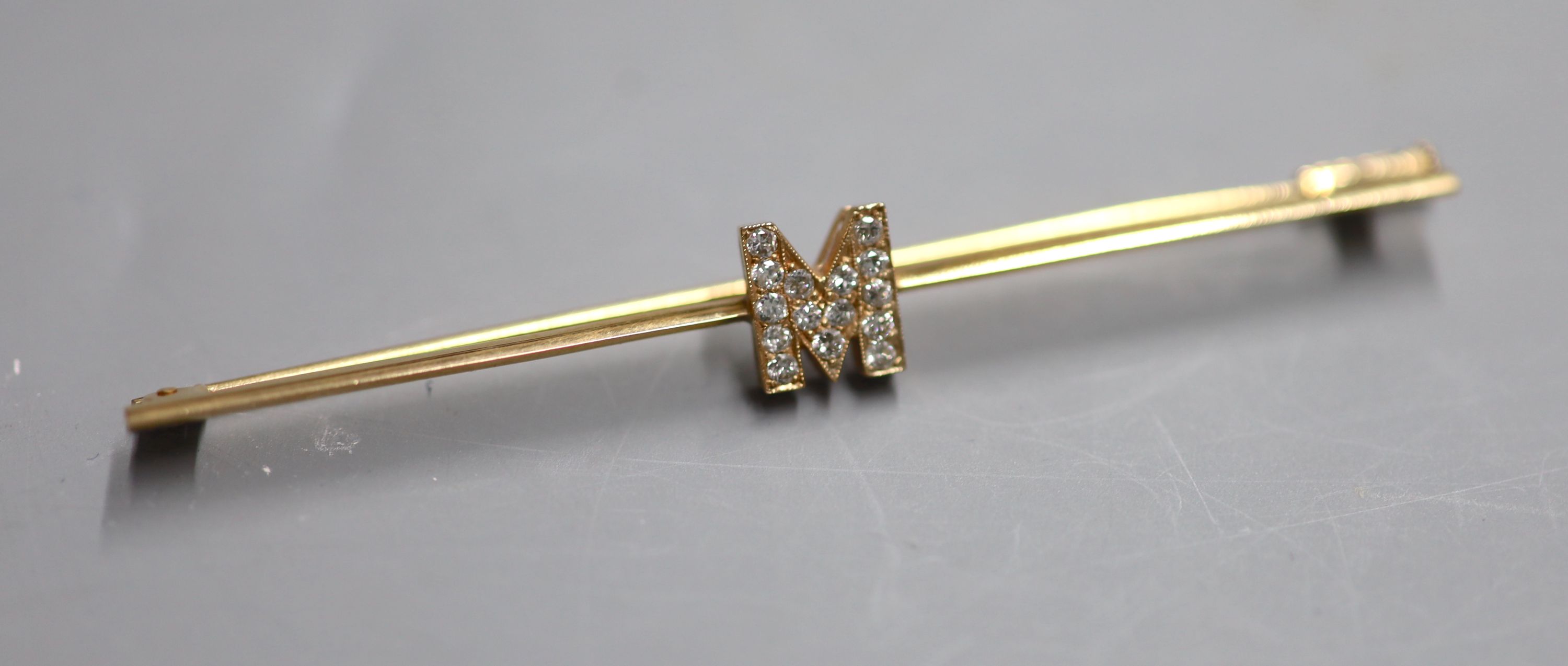 A yellow metal and diamond set initial M bar brooch, 77mm, gross 4.6 grams.